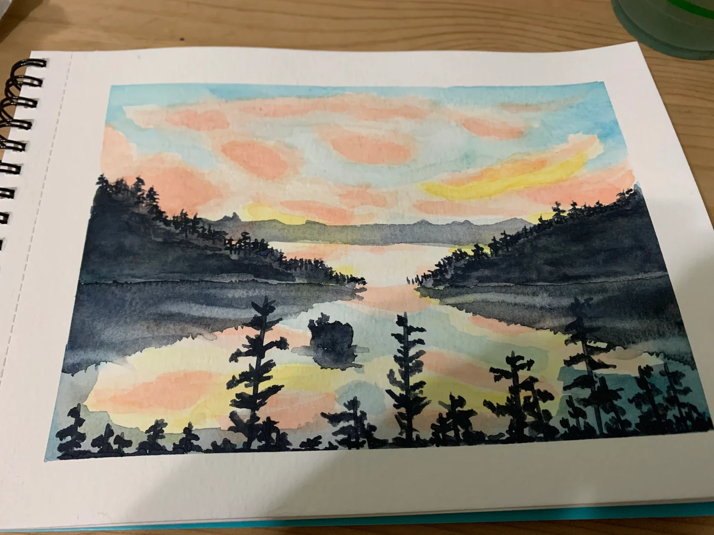 Sketchbook painting of a misty lake framed by dark trees under a peach and blue sky.
